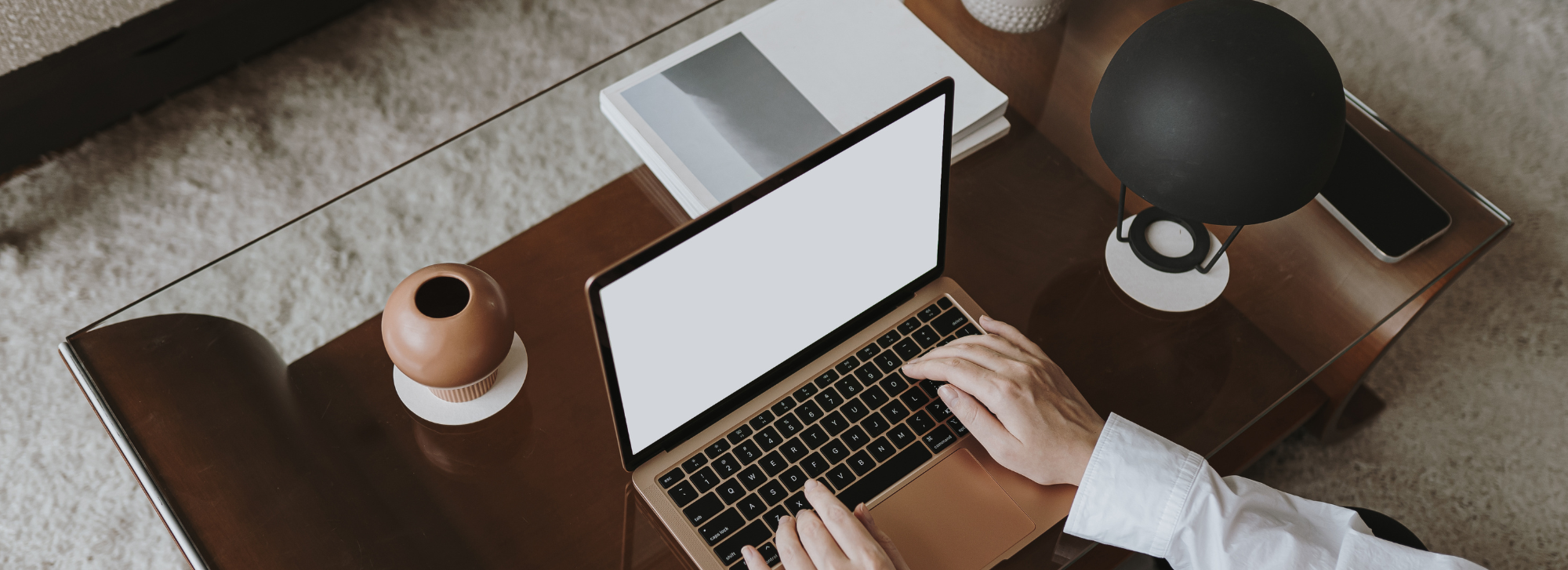 Person using their computer on the coffee table with a lamp next to them.