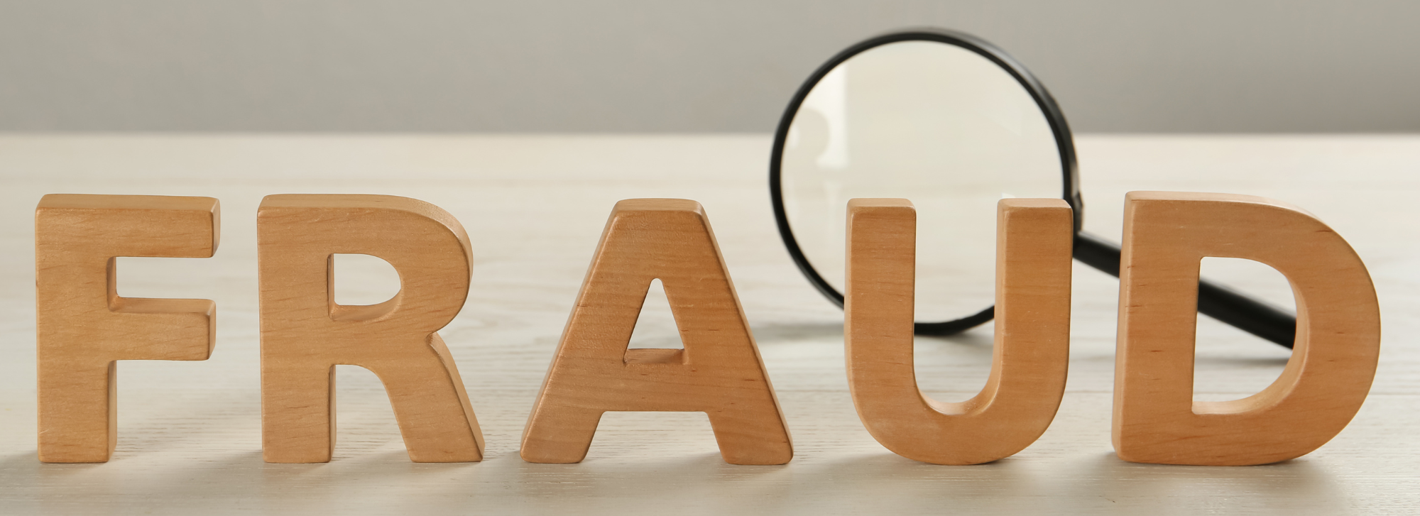 Wooden blocks that spell the word fraud with a magnifying glass in the background