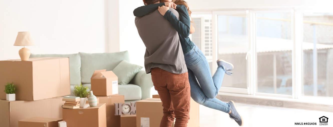 Man and a woman hugging in a living room surrounded by moving boxes.