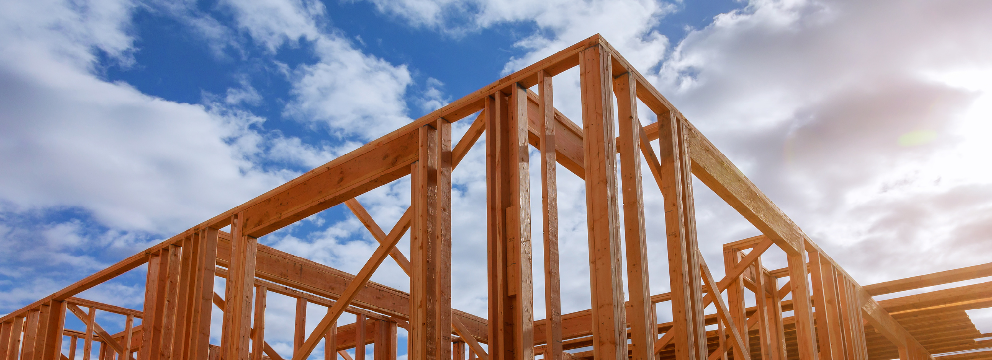 Image is of the trusses of someone's home and in the background is a blue cloudy sky.