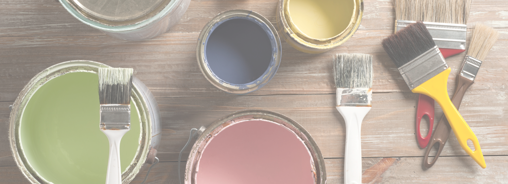 Different paint colors and paint brushes sitting on a wooden table.