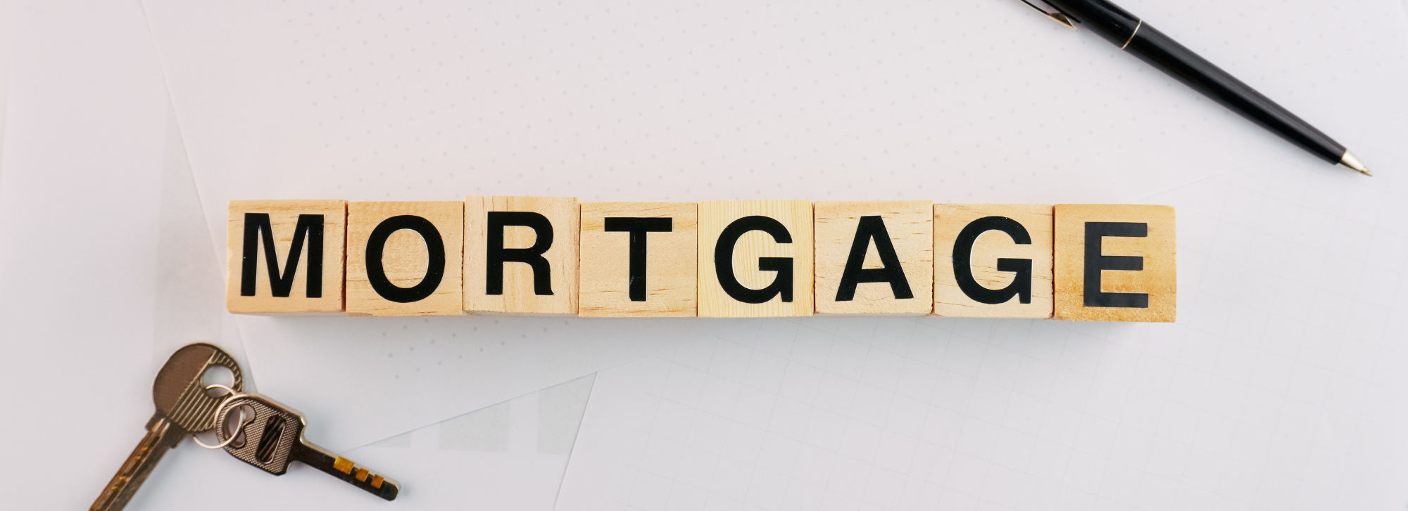 The word mortgage is written in scrabble tiles and there is a set of keys and a pen sitting next to it.