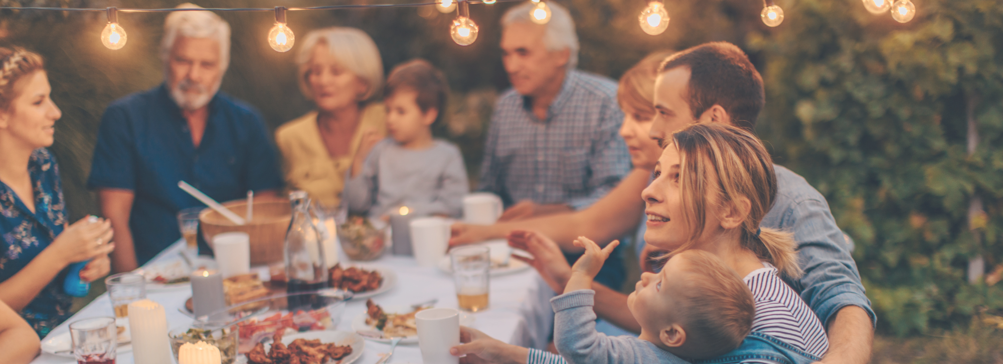 A family sitting around a table eating outside under decorative lights.